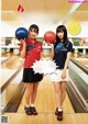 A couple of women standing next to each other holding bowling balls.