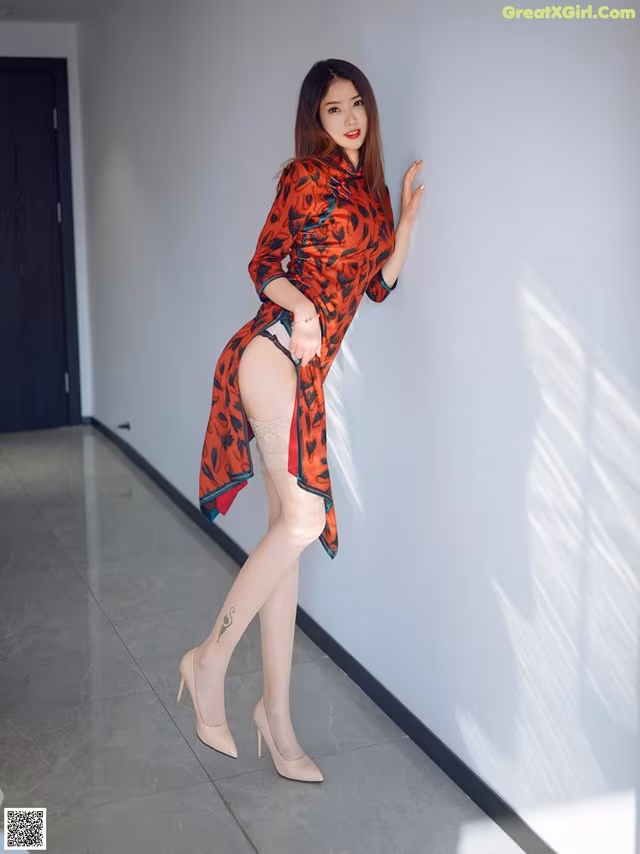 A woman in a red and black dress leaning against a wall.