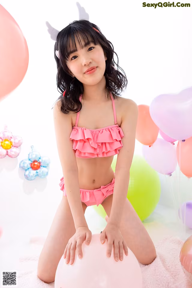A young woman in a pink bikini sitting on a pink blanket surrounded by balloons.