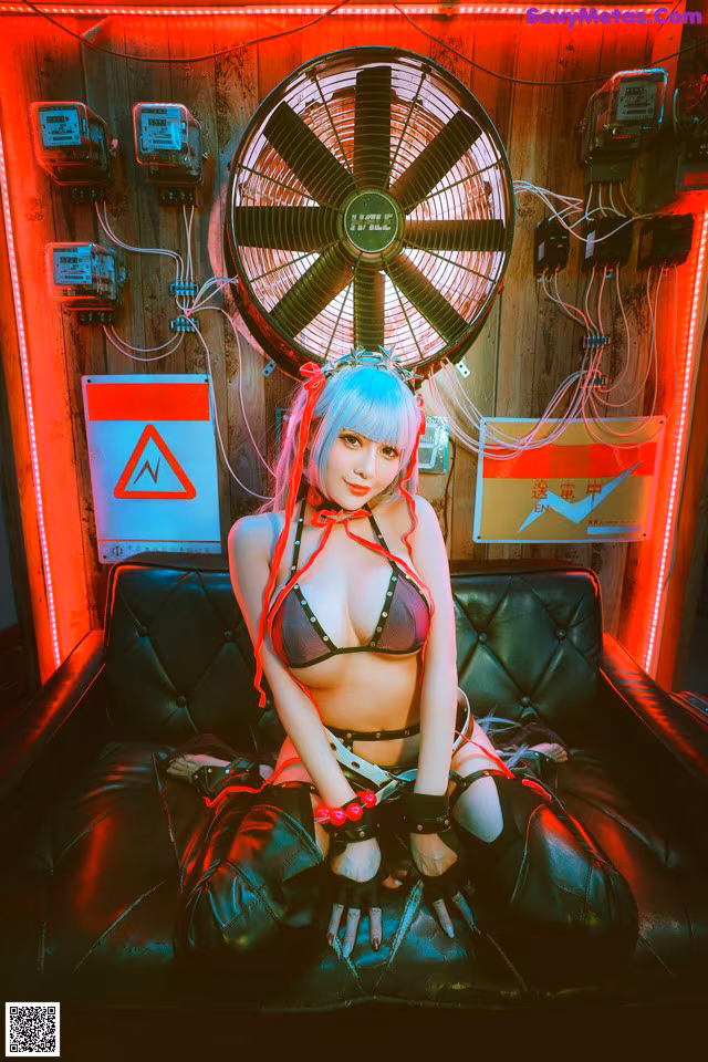 A woman sitting on a couch in front of a fan.