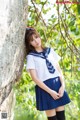 A woman in a school uniform leaning against a tree.