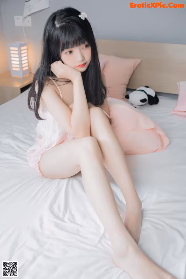 A woman sitting on top of a bed in a pink dress.