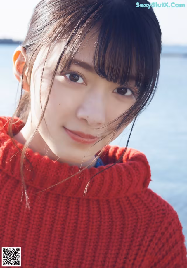 A woman in a red sweater standing by the water.
