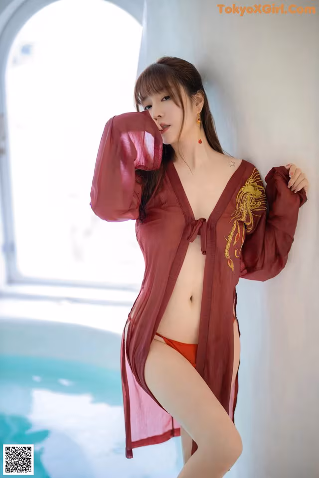 A woman in a red robe leaning against a wall.
